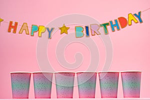 Pink party cups with happy birthday garland on pink background