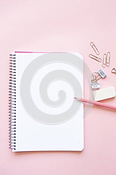 pink pencil and stationery items on notepad with blank page and on pink background