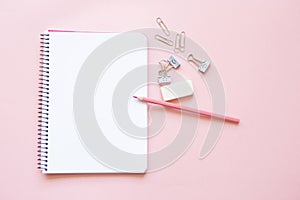 pink pencil and stationery items on notepad with blank page and on pink background