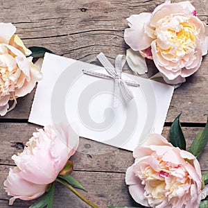 Pink peonies flowers and empty tag on aged wooden background.