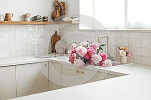 Pink peony and roses flowers in modern kitchen interior, summer floral arrangement. Beautiful peonies in sink on background of