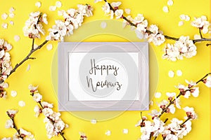 Pink photo frame and sprigs of white apricot tree with flowers on yellow background.