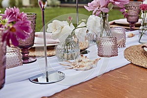 Pink picnic aesthetic table setting, flowers arrangement, shells close up. Cozy setup with flowers and candles