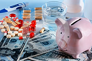 A pink pig piggy bank is on the dolor banknotes. There are scattered tablets and capsules. Concept, dear medicine.