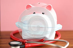 Pink pig piggy bank in protective mask and stethoscope stands on table