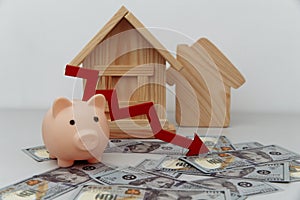 Pink piggy bank with arrow down and wooden house models on dollar banknotes, Saving or loan for buy house or real estate