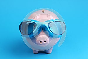 Pink piggy bank with blue swimming goggles on blue background like swimmer