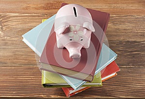 Pink Piggy bank with books on wooden background. Concept of funding education