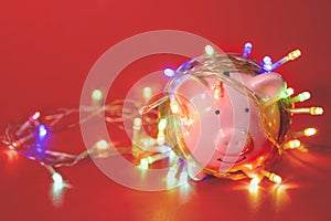 Pink piggy bank with Christmas string lights on happy December festival in Red background, Enjoy savings for spending money on the