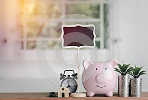 Pink piggy bank  coin money  alarm clock  house model  Toy cars  and signs  all placed on the table In a white office.  the