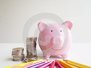Pink piggy bank with coins pile and Bright colored pencils, Saving money for future plan and retirement fund concept