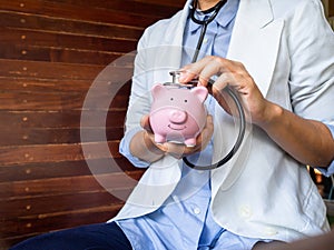 Pink piggy bank examined by a female doctor. Using stethoscope. Wooden background for copy space. Financial Health concept