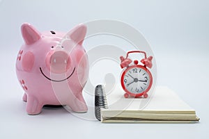 Pink piggy bank Expense Book And red alarm clock The idea of saving money to buy a house for the future, accumulating a small