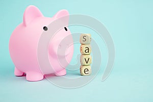 Pink piggy bank with geometric wood blocks cube adt text SAVE on blue background. Saving money concept