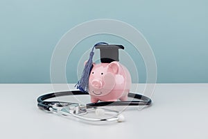 Pink piggy bank with graduation cap and stethoscope as a concept image of the costs of medical education