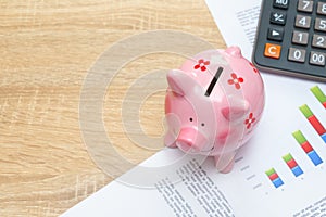 Pink piggy bank with graph and calculator on wooden desk - growing interest rate concept