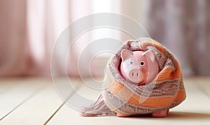 A pink piggy bank money box wrapped up warm with a scarf. Winter heating bills concept