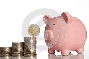 Pink piggy bank and stack of coins growing up with two euro coin