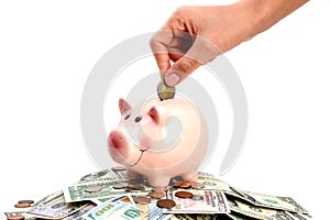 Pink piggy bank standing on a pile of coins and bills, suggesting money savings concept