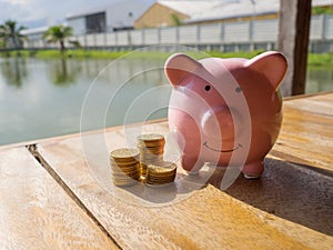 Pink piggy bank standing on wooden with gold coins pile and water background, Saving money for future plan and retirement fund