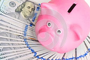 pink piggy bank stands on a fan of a pile of american dollars on a white background