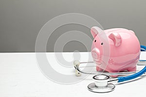 Pink piggy bank and stethoscope on a gray background. Concept of how to save on health insurance or personal insurance