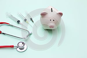 Pink piggy bank with stethoscope and syringe