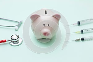 Pink piggy bank with stethoscope and syringe