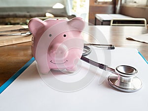 Pink piggy bank and stethoscope on wooden table, to demonstrate for saving money for future. Financial Health concept