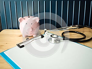 Pink piggy bank and stethoscope on wooden table, to demonstrate for saving money for health care