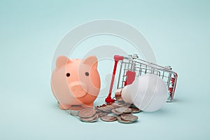 Pink piggy bank, trolley and light bulb on blue background, power savings concept