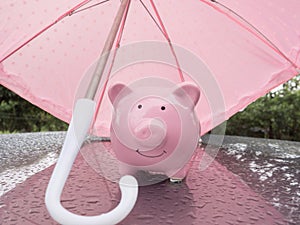 Pink Piggy bank with umbrella On a rainy day Saving money for any storm problem will come concept for finance, insurance,