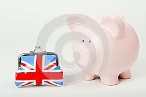 Pink piggy bank with Union Jack purse on white background.