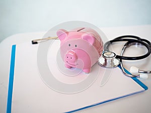 Pink piggy bank on white doctor`s chart and stethoscope in copy space background.