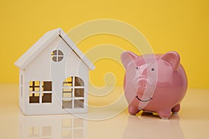 Pink piggy bank with white wooden house on yellow background
