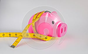 Pink piggy bank with yellow measuring tape tied around ears , struggle for waist