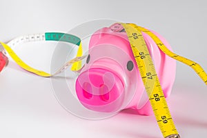 Pink piggy bank with yellow measuring tape tied around ears , struggle for waist