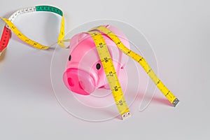 Pink piggy bank with yellow measuring tape tied around ears , struggle for waist