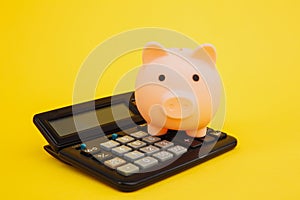 Pink piggy or coin bank or piggybank or money box on calculator - finance and savings concept on yellow background