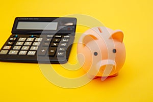 Pink piggy or coin bank or piggybank or money box and calculator - finance and savings concept on yellow background