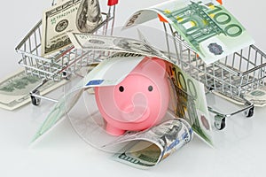 Pink piggy money box in pile of dollar and euro banknotes