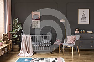 Pink pillow on grey armchair next to kid`s bed with blanket in b