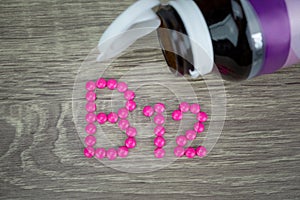 Pink pills forming shape to B12 alphabet on wood background