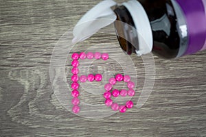 Pink pills forming shape to Fe alphabet on wood background