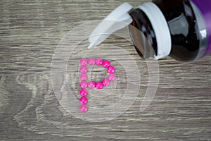 Pink pills forming shape to P alphabet on wood background