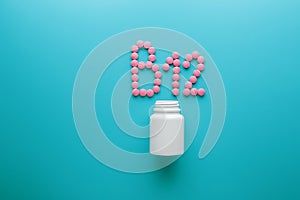 Pink pills in the shape of the letter B12 on a blue background, spilled out of a white can