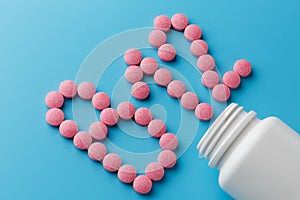 Pink pills in the shape of the letter B12 on a blue background, spilled out of a white can