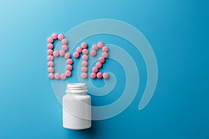 Pink pills in the shape of the letter B12 on a blue background, spilled out of a white can