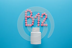 Pink pills in the shape of the letter B12 on a blue background, spilled out of a white can