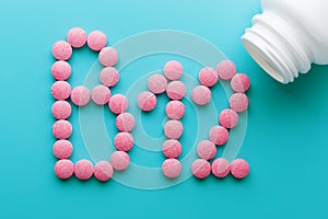 Pink pills in the shape of the letter B12 on a blue background, spilled out of a white can